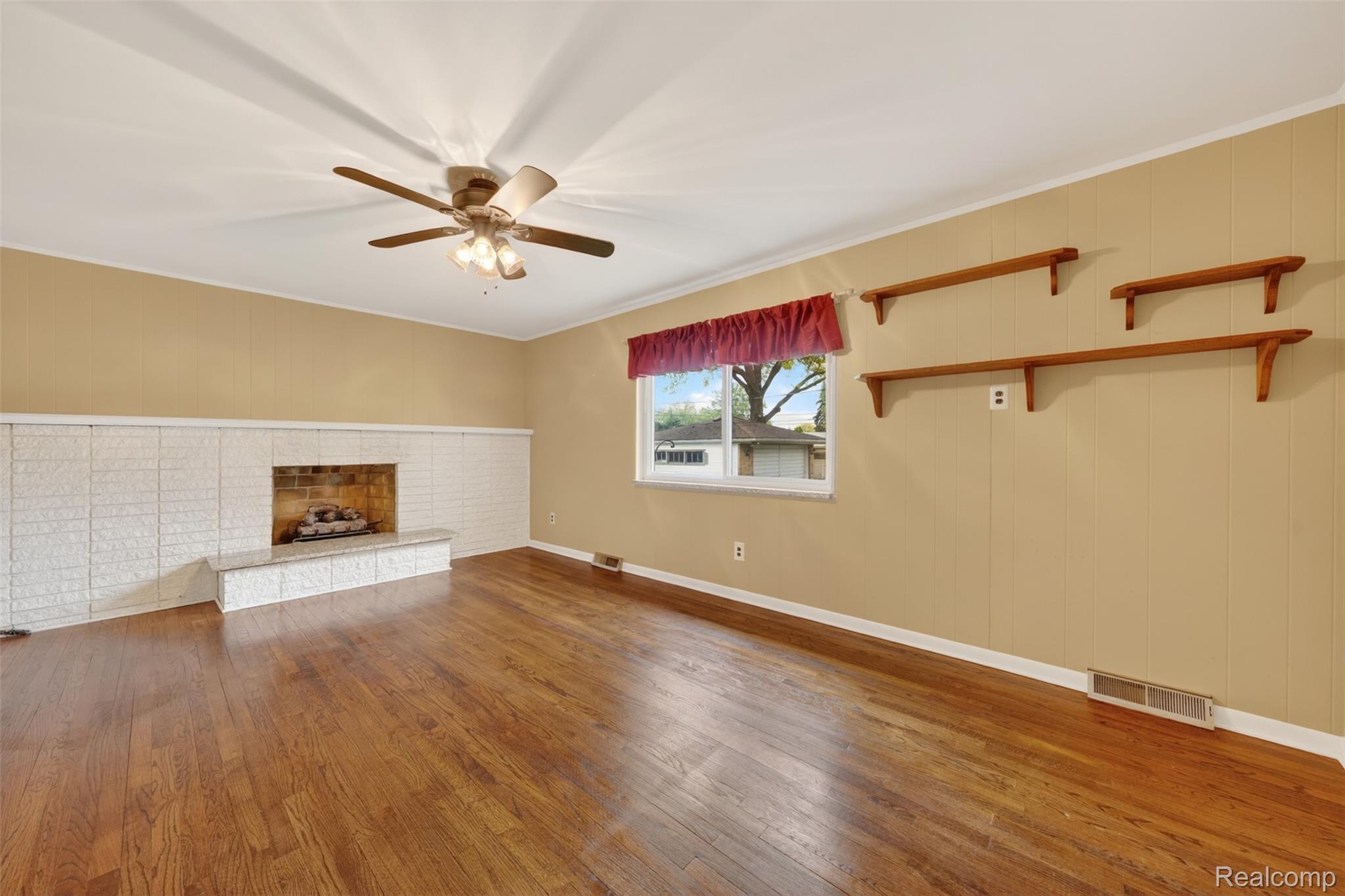 12014 Common Road Warren, MI 48093 - Photo 15 of 30 Unfurnished living room featuring hardwood / wood-style flooring, ceiling fan, a brick fireplace, and crown molding