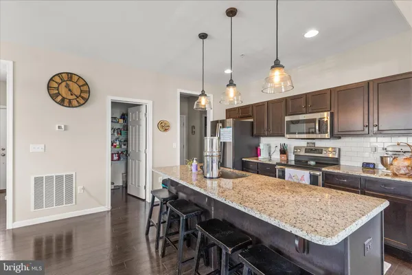 a kitchen with stainless steel appliances granite countertop a stove top oven a refrigerator a sink a dining table and chairs with wooden floor