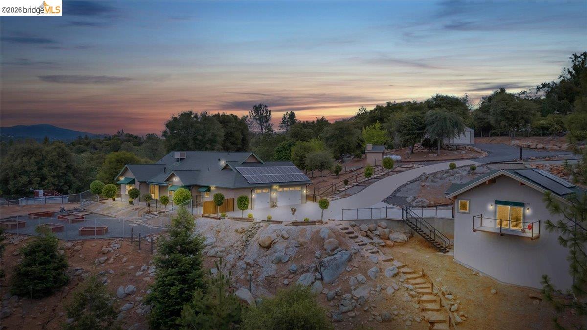 Hillside property featuring a main residence, separate structure with balcony, paved driveway, and multiple solar panel arrays