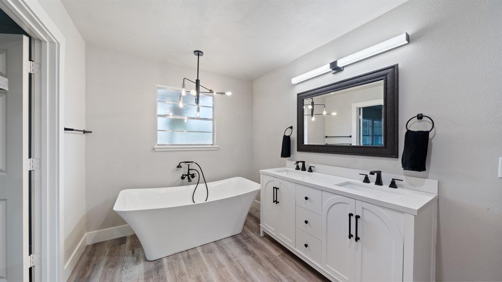 129 King Arthur Road Mabank, TX 75156 - Photo 10 of 33 The bathroom features a freestanding tub, a window with privacy glass, a double vanity with white cabinetry and dark hardware, and a dark framed mirror with overhead lighting