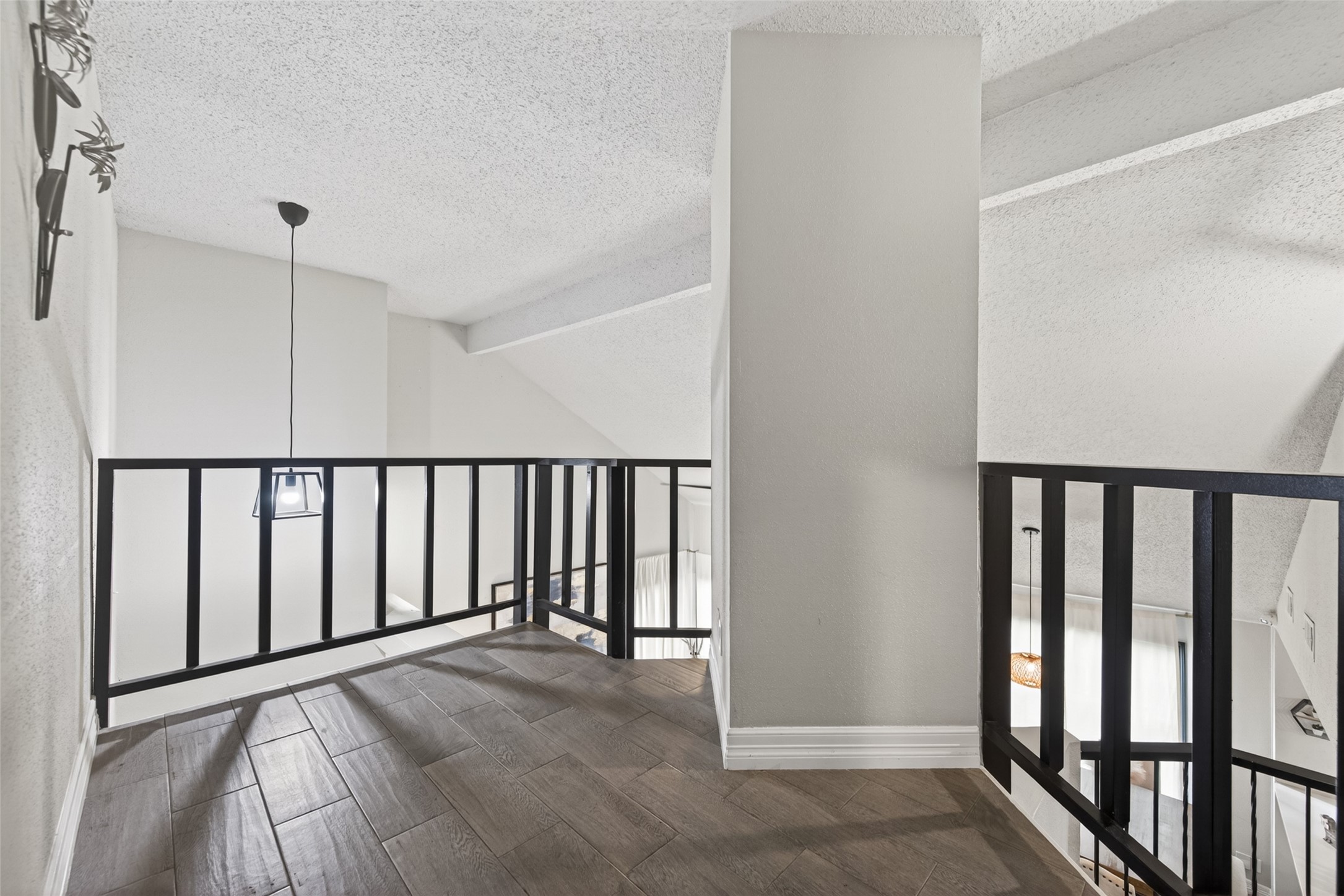 18446 North Willow Bluff Road Katy, TX 77449 - Photo 29 of 33 This photo showcases a modern loft area with a high ceiling and a sleek black railing. The space features wood-look flooring and is well-lit with a hanging pendant light, offering a stylish and open feel.