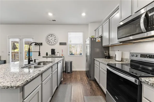 a kitchen with stainless steel appliances granite countertop a stove top oven a sink dishwasher a refrigerator and a oven with wooden floor