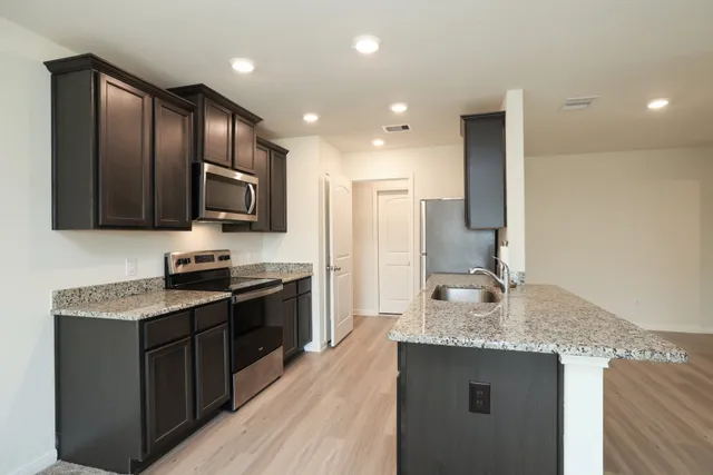 a kitchen with kitchen island granite countertop stainless steel appliances a sink stove refrigerator and cabinets