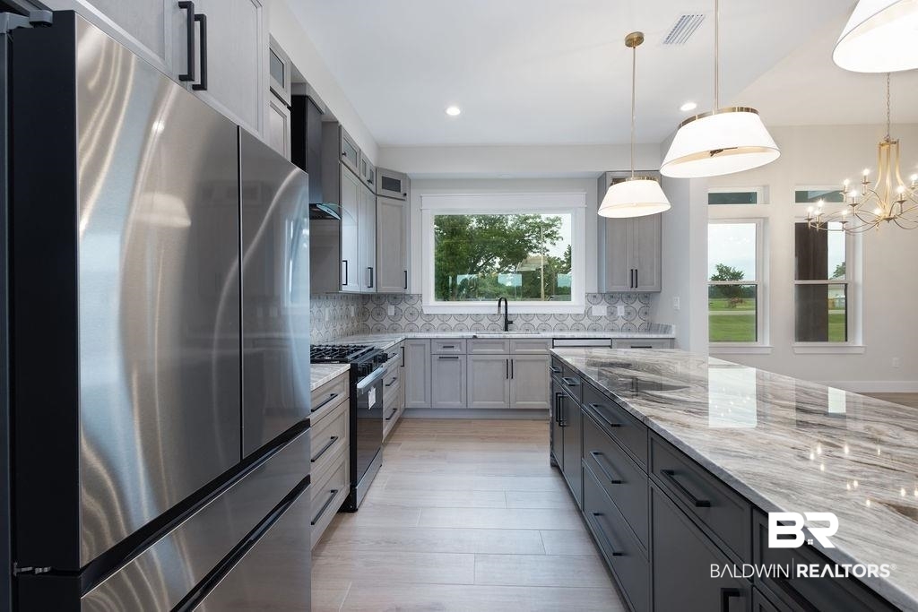 13066 Gopher Court Elberta, AL 36530 - Photo 6 of 38 Gourmet kitchen featuring a large island with a polished granite countertop, stainless steel appliances, light gray cabinetry, and contemporary pendant lighting.