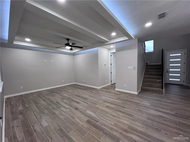 a view of an empty room with wooden floor and a ceiling fan