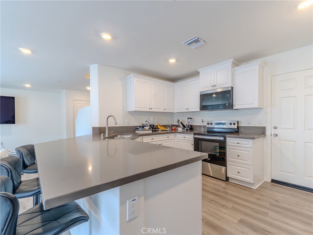 25602 Pne Rdg Road Homeland, CA 92548 - Photo 12 of 35 a large kitchen with granite countertop a stove a sink a refrigerator and white cabinets with wooden floor