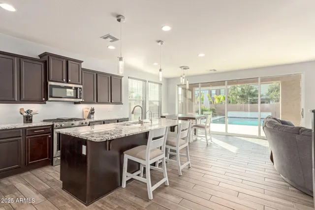 a kitchen with stainless steel appliances granite countertop a stove top oven a sink dishwasher a dining table and chairs with wooden floor