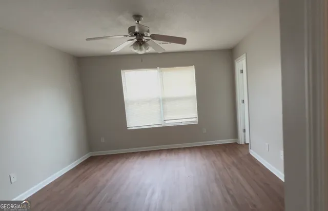 an empty room with wooden floor chandelier fan and windows