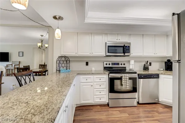 a kitchen with stainless steel appliances granite countertop a stove top oven a sink a dining table and chairs with wooden floor