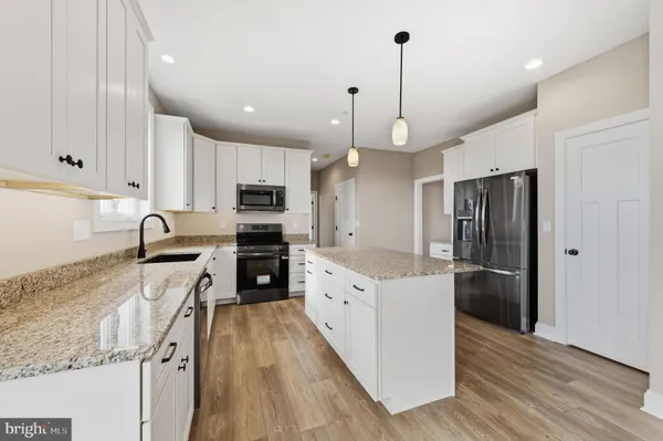 a large kitchen with stainless steel appliances granite countertop a refrigerator a oven a sink and white cabinets with wooden floor