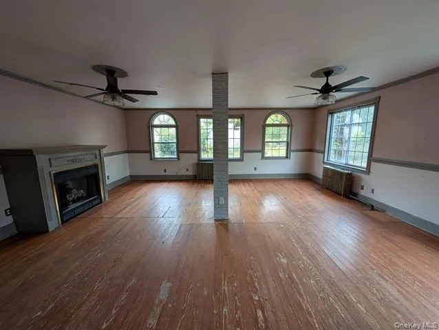 an empty room with wooden floor a chandelier a fireplace and windows