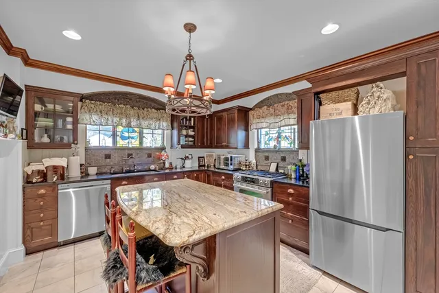 a kitchen with stainless steel appliances granite countertop a refrigerator a sink dishwasher a stove and a dining table with wooden floor