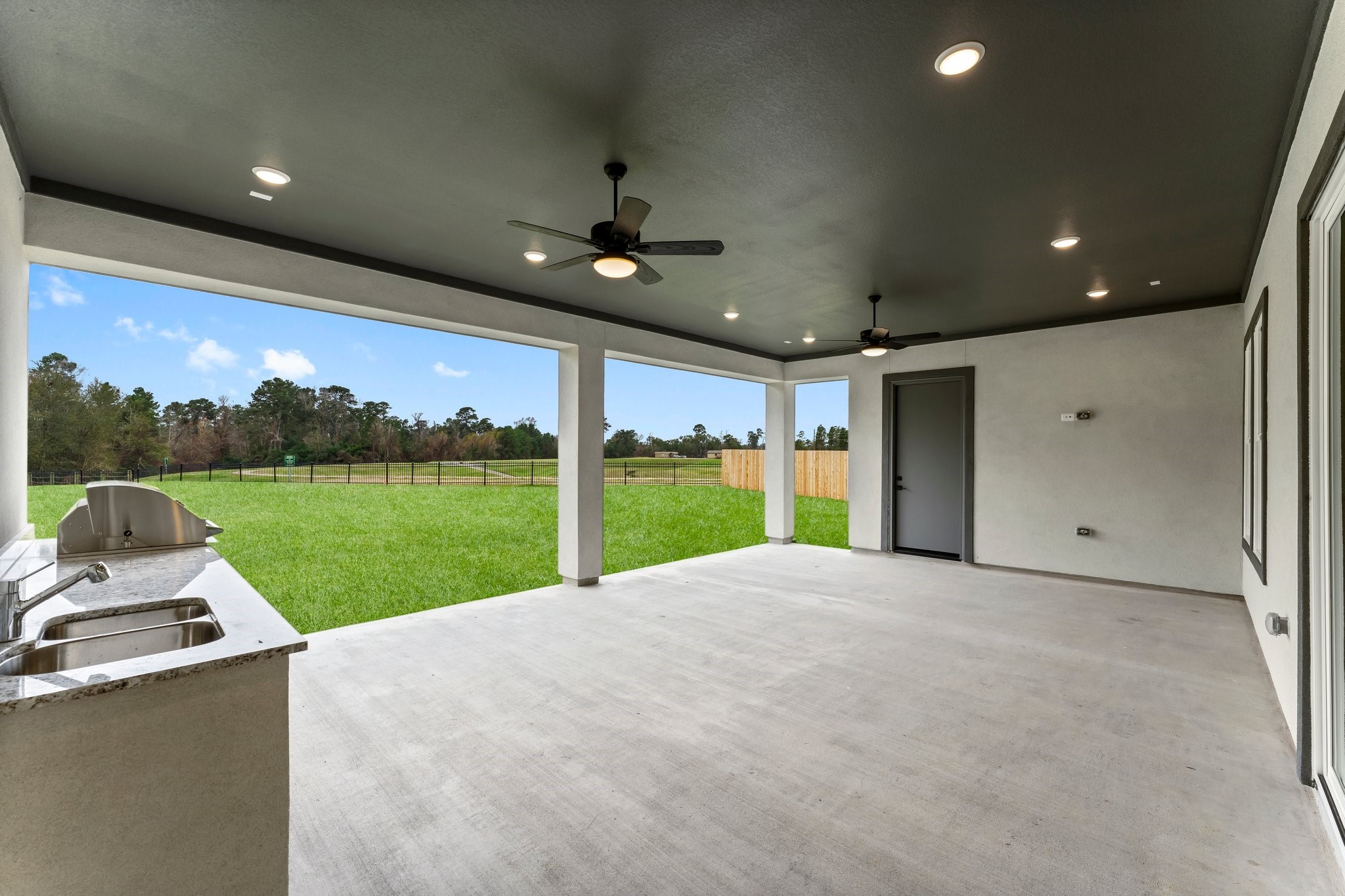 7315 Julie Pond Lane Spring, TX 77389 - Photo 42 of 48 This photo showcases a spacious covered patio with ceiling fans and recessed lighting, overlooking a large, fenced backyard. An outdoor kitchen with a sink and countertop provides a perfect space for entertaining.