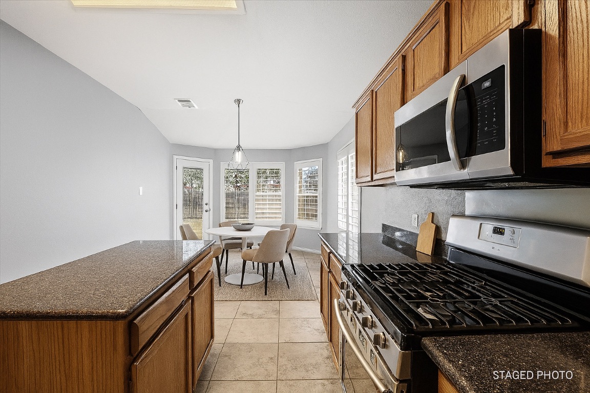 13438 Moscow Trail Austin, TX 78729 - Photo 5 of 40 Virtually Staged
Kitchen featuring appliances with stainless steel finishes, brown cabinets, and dark stone counters