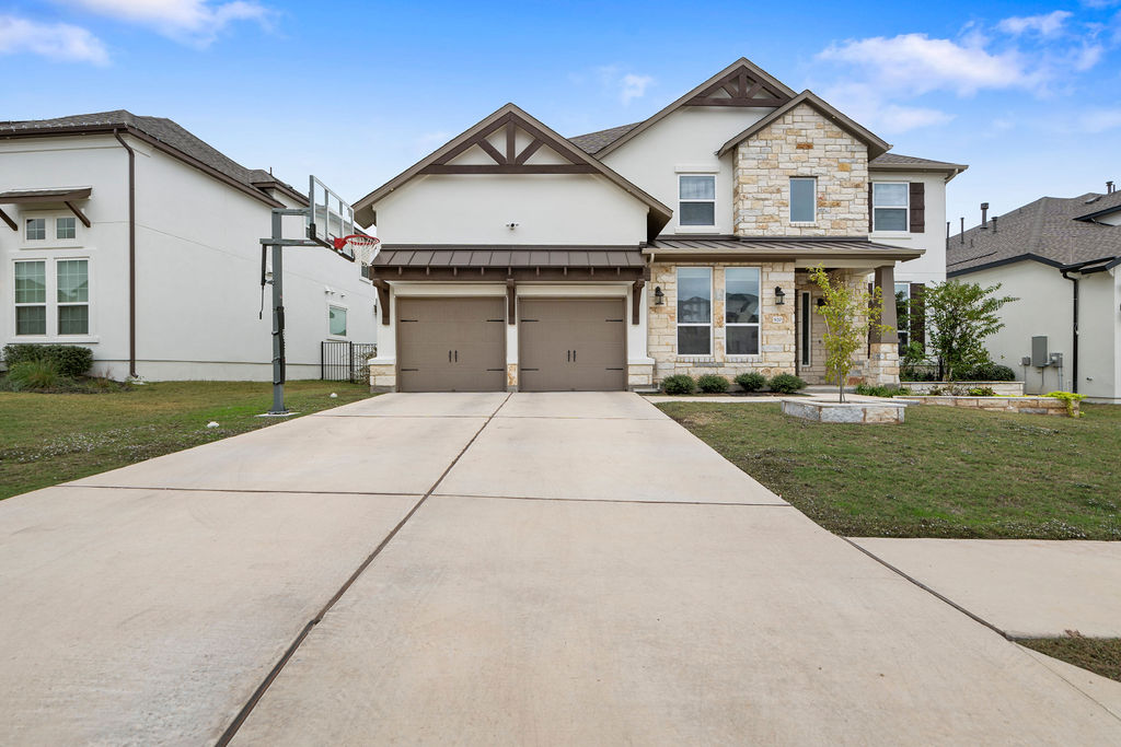 View of front of home with a front lawn, a standing seam roof, a metal roof, stone siding, and driveway