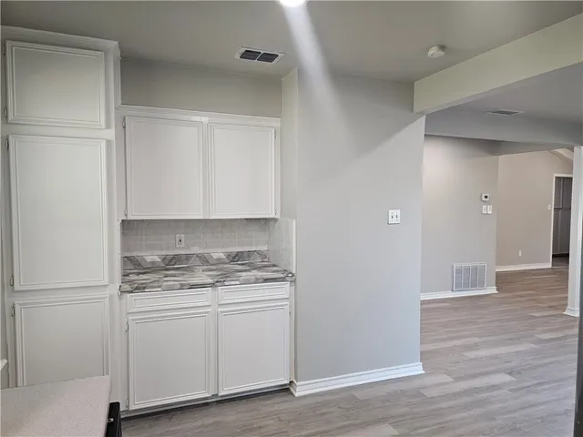 an empty room with wooden floor and a kitchen
