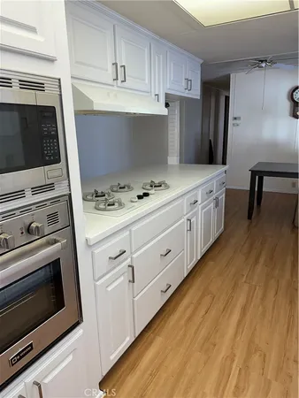 a view of an empty room with wooden floor and a kitchen