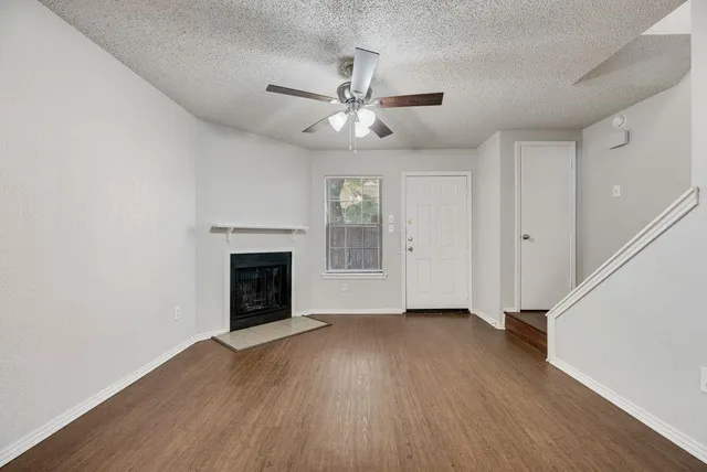 a view of an empty room with wooden floor fireplace and a window