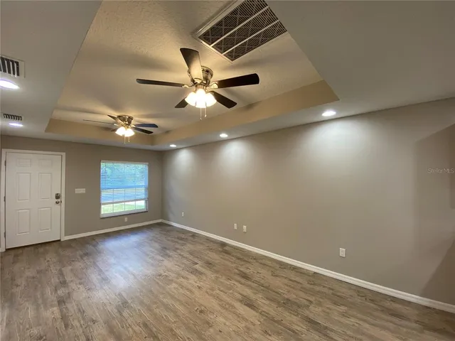 an empty room with wooden floor chandelier fan and windows