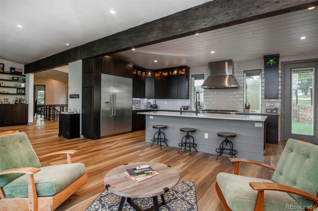 a kitchen with stainless steel appliances kitchen island granite countertop a refrigerator a stove a sink a dining table and chairs with wooden floor