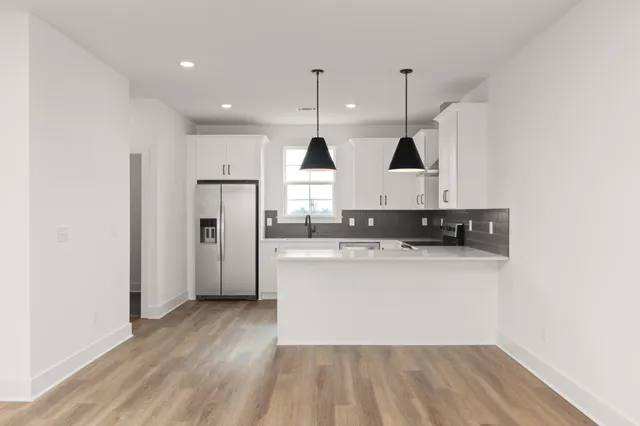 a kitchen with stainless steel appliances granite countertop a sink a stove a refrigerator and white cabinets with wooden floor