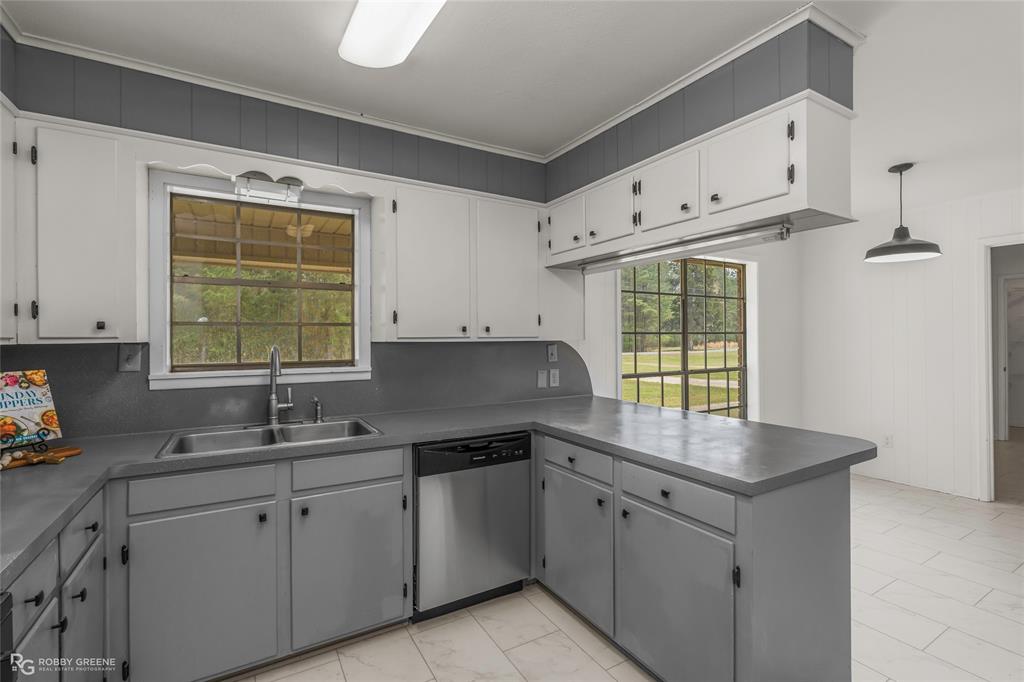 1303 Young Road Benton, LA 71006 - Photo 14 of 34 Kitchen featuring stainless steel dishwasher, a peninsula, dark countertops, gray cabinetry, and wood walls