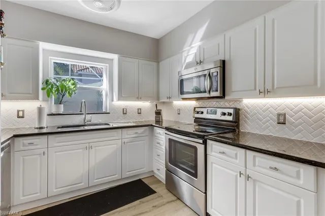 a kitchen with granite countertop white cabinets sink and stainless steel appliances
