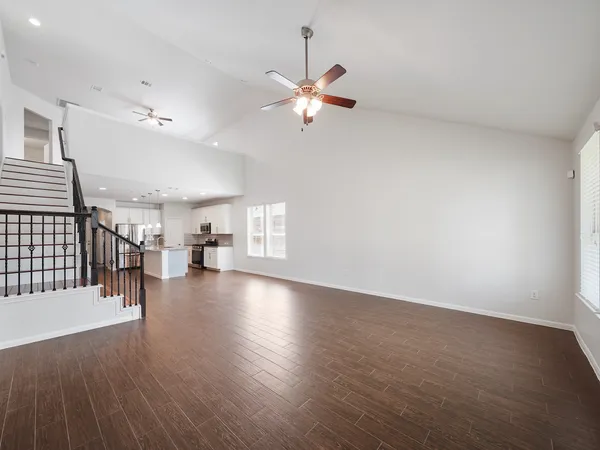 an empty room with wooden floor chandelier fan and windows