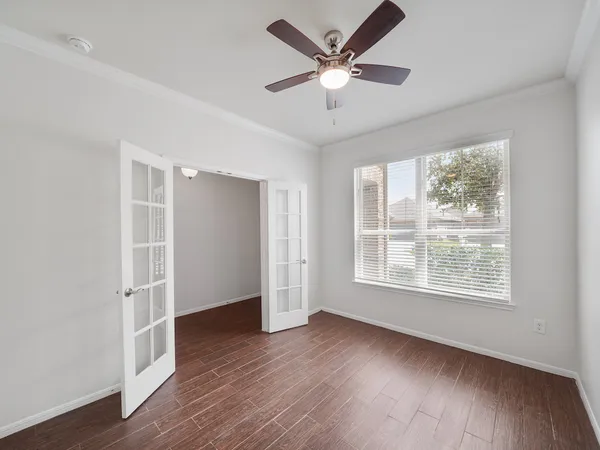 an empty room with wooden floor chandelier fan and windows