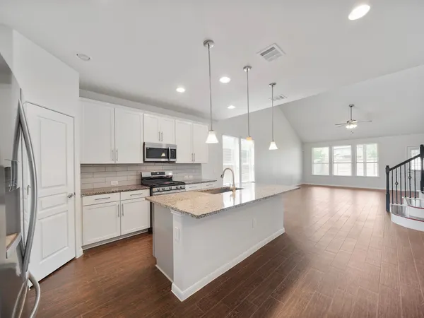 a large kitchen with stainless steel appliances granite countertop a stove a sink dishwasher a refrigerator white cabinets and wooden floor next to a window