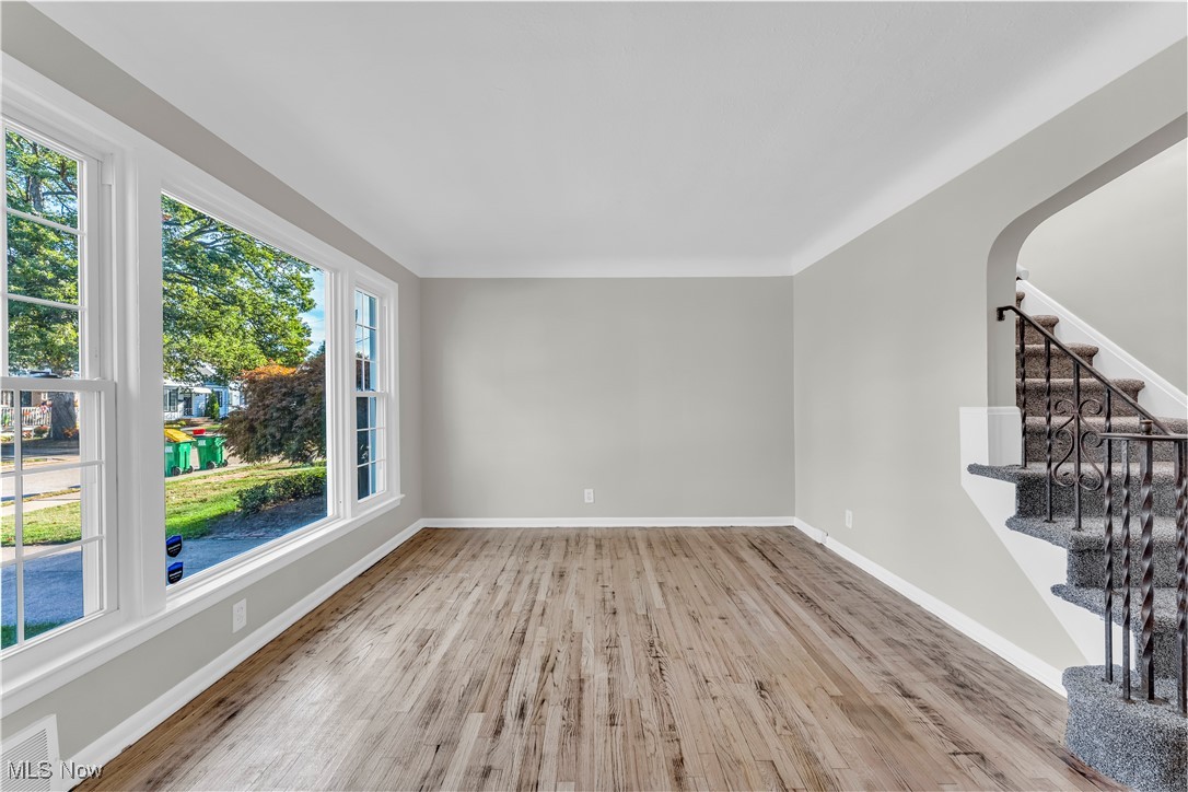 Unfurnished living room with stairway, light wood-style flooring, and arched walkways