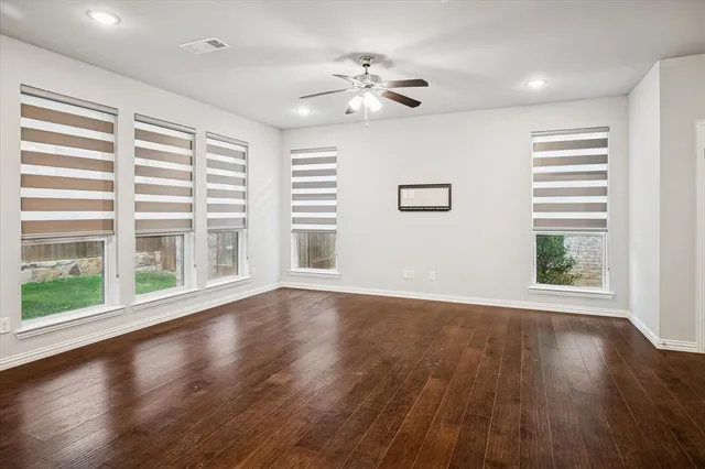 a view of an empty room with wooden floor and a kitchen