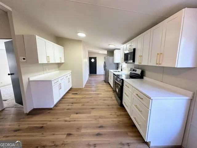 a kitchen with stainless steel appliances a stove top oven a sink a refrigerator white cabinets and wooden floor