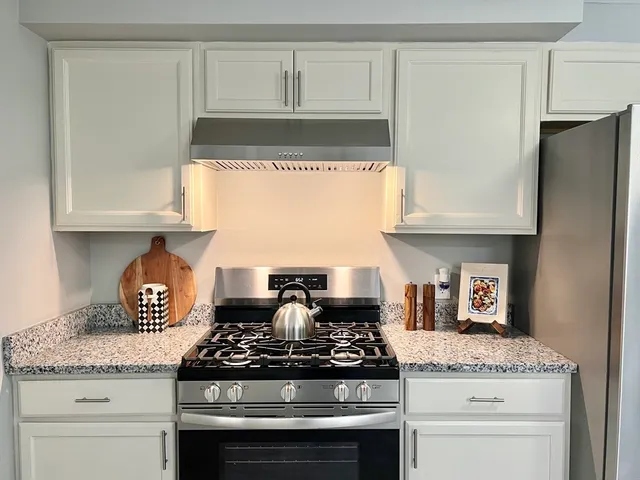 a kitchen with granite countertop a stove and a white cabinets
