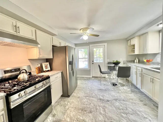 a kitchen with stainless steel appliances granite countertop a stove a sink dishwasher a refrigerator and white cabinets with wooden floor