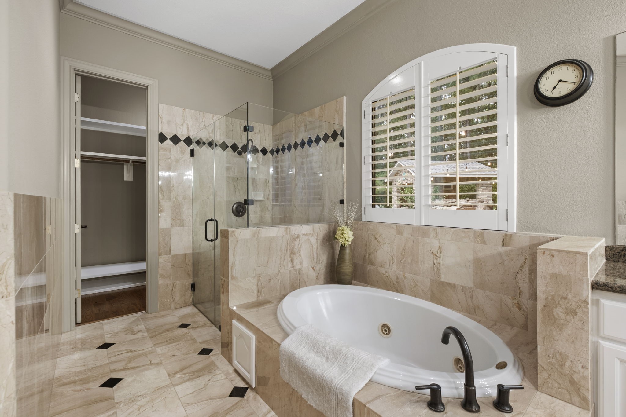 20010 Timber Ridge Drive Magnolia, TX 77355 - Photo 21 of 50 This primary en-suite bath features elegant marble tile, a spacious glass-enclosed shower, a luxurious jetted tub, and a large window with plantation shutters. Two walk-in closets provide ample storage, and the room is accented with neutral tones for a serene atmosphere.
