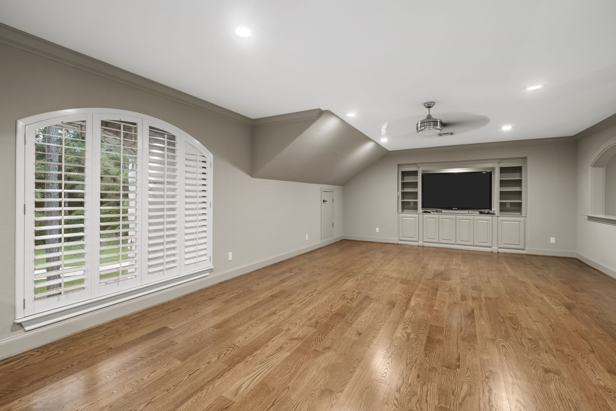 20010 Timber Ridge Drive Magnolia, TX 77355 - Photo 27 of 50 Perched upstairs, this versatile game room offers the perfect blend of fun and function. This spacious room features hardwood floors, a large window with shutters, built-in shelving with a TV area, and recessed lighting, offering a modern and airy feel.
