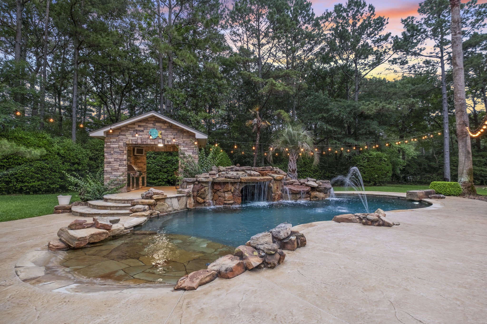 20010 Timber Ridge Drive Magnolia, TX 77355 - Photo 35 of 50 Imagine spending your summer here in this serene backyard oasis featuring a rustic salt-water pool, a grotto with waterfall, and a diving rock, all surrounded by lush greenery and mature trees. The expansive patio provides plenty of space for lounging, and the outdoor kitchen is conveniently located nearby.