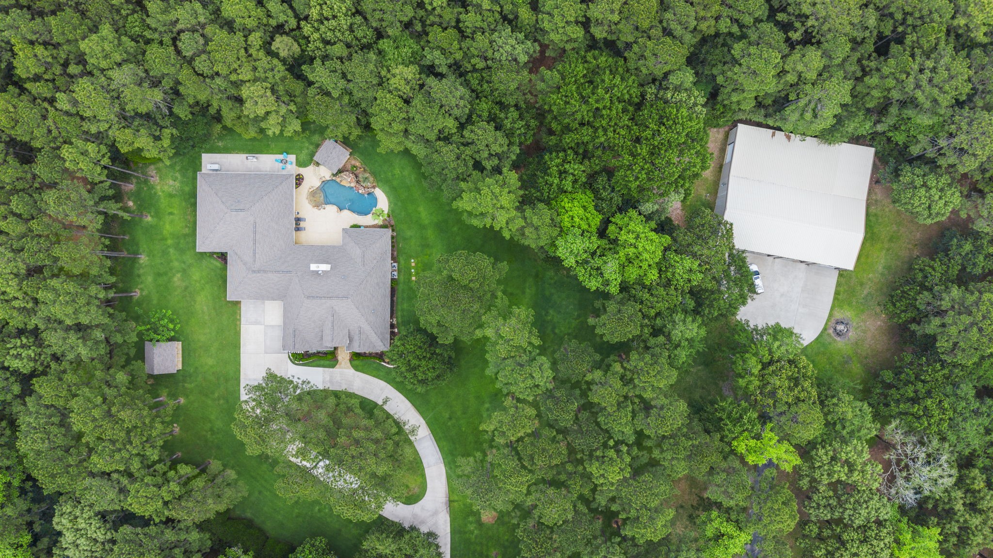 20010 Timber Ridge Drive Magnolia, TX 77355 - Photo 47 of 50 From above, this remarkable property reveals its full grandeur—an expansive estate set on 10 wooded acres, offering a rare blend of privacy and possibility. The impressive main home sits as the centerpiece, surrounded by a canopy of mature trees, while a substantial workshop adds incredible versatility for work or recreation.