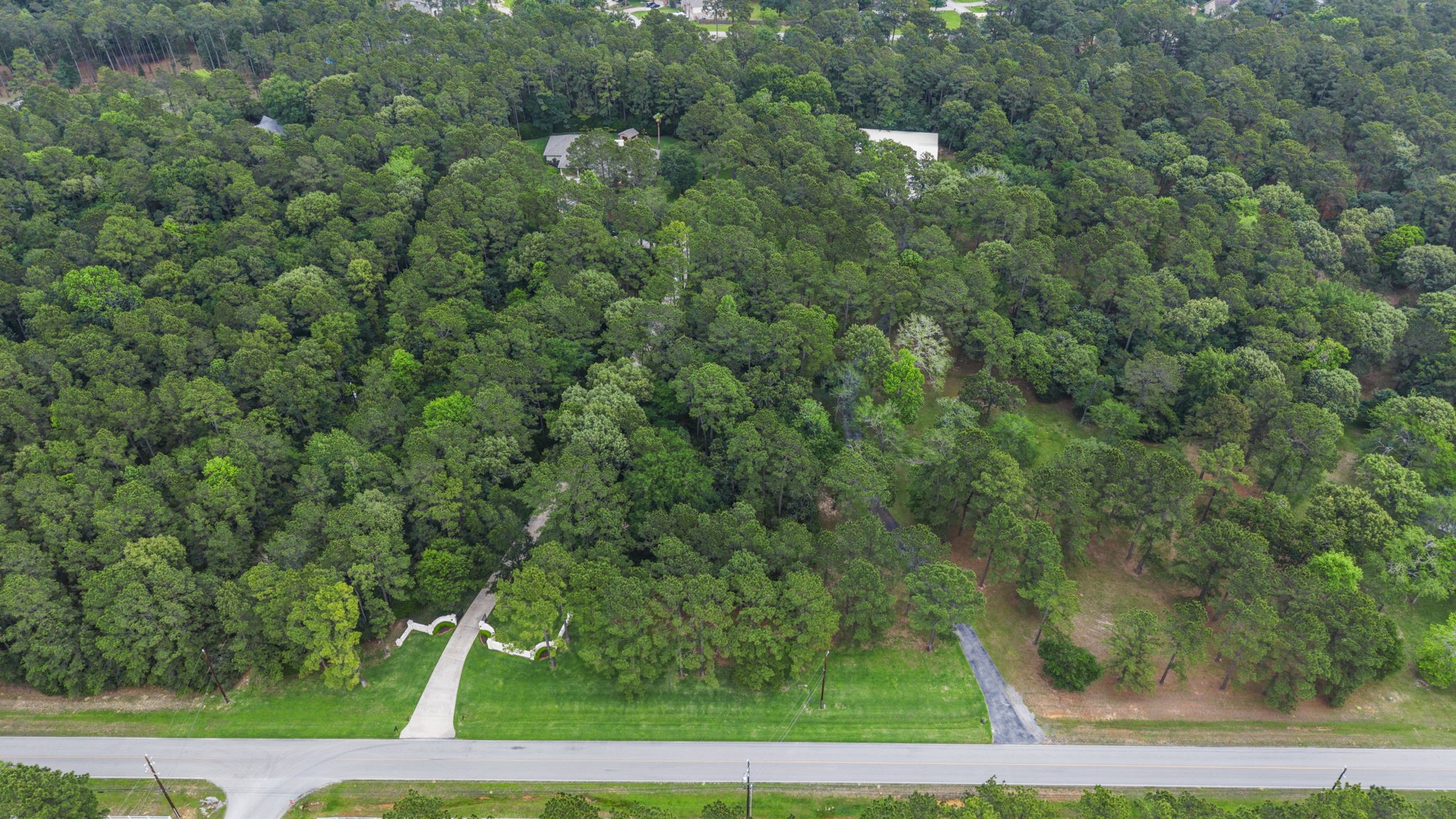 20010 Timber Ridge Drive Magnolia, TX 77355 - Photo 48 of 50 Winding clearings and natural surroundings create a peaceful, park-like setting, showcasing the scale, seclusion, and beauty of this one-of-a-kind retreat. The property also backs to scenic equestrian trails, offering direct access for riding and outdoor enjoyment. This view very nicely shows the two driveways into the property - the gated drive leading to the home and the blacktop driveway leads to the workshop.