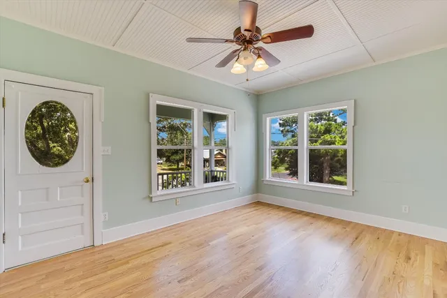 an empty room with wooden floor fan and windows