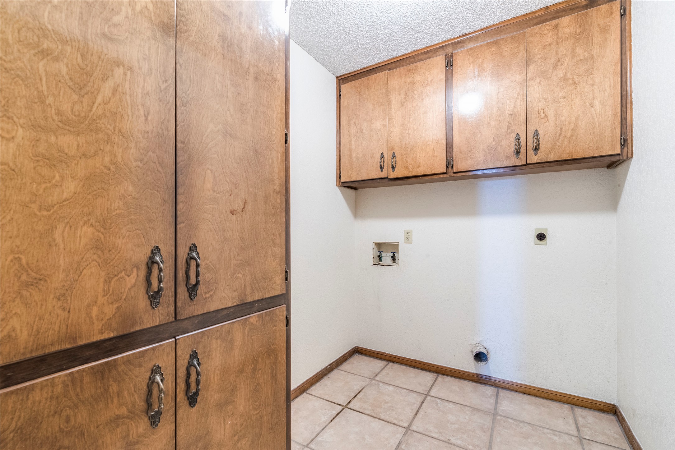13505 Broadmeade Avenue Austin, TX 78729 - Photo 18 of 21 Laundry room with a textured ceiling, cabinet space, hookup for a washing machine, light tile patterned flooring, and electric dryer hookup
