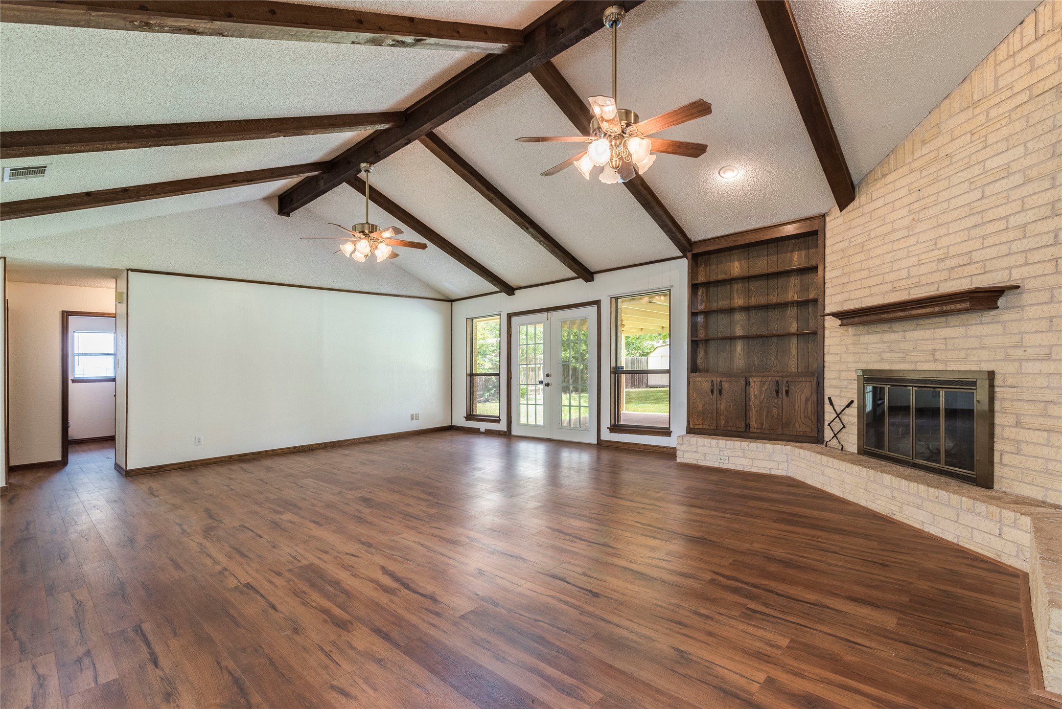 13505 Broadmeade Avenue Austin, TX 78729 - Photo 5 of 21 Unfurnished living room featuring a textured ceiling, french doors, built in shelves, a brick fireplace, and dark wood-type flooring