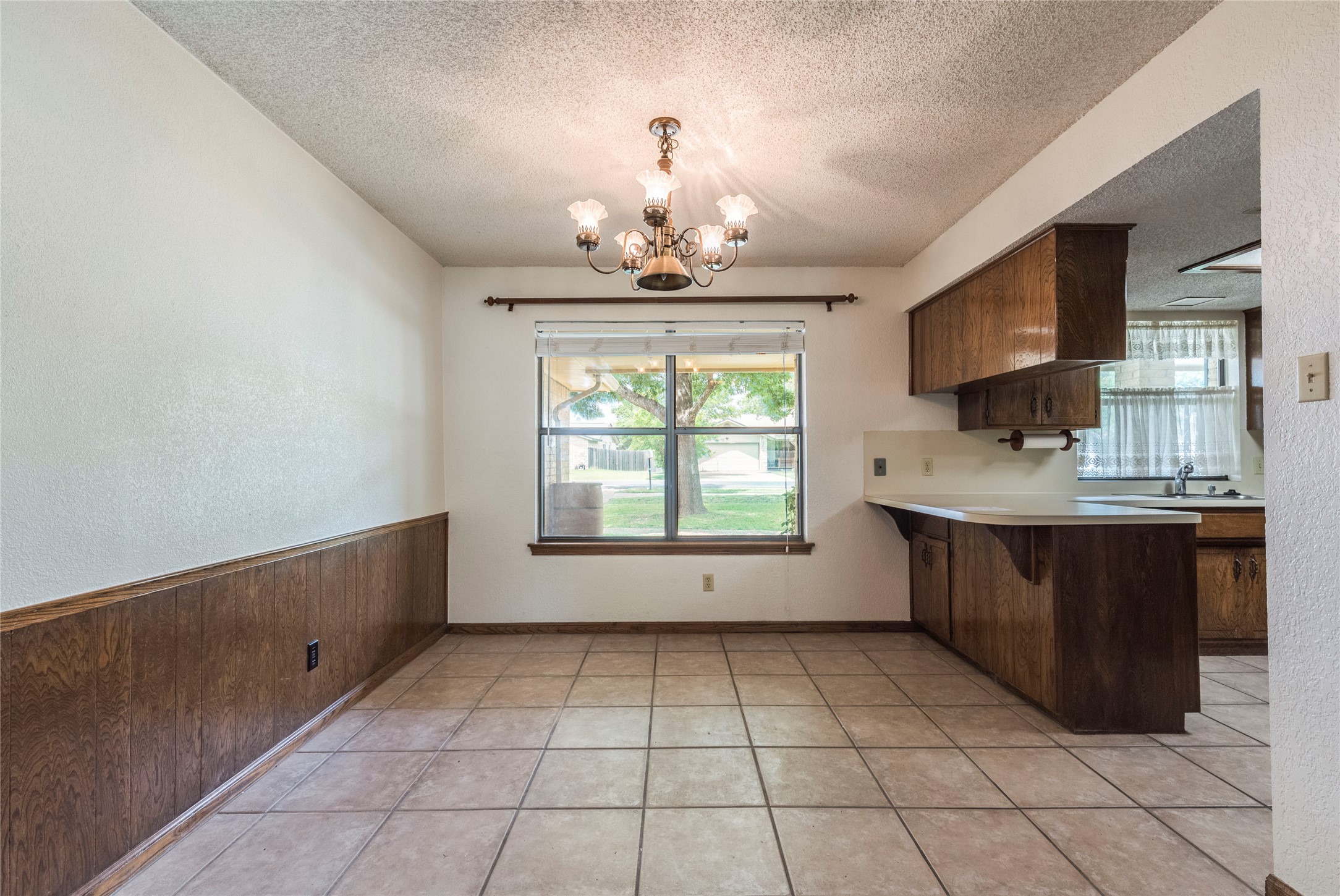 13505 Broadmeade Avenue Austin, TX 78729 - Photo 6 of 21 Kitchen featuring a peninsula, light countertops, suspended lighting, a textured ceiling, and wood walls