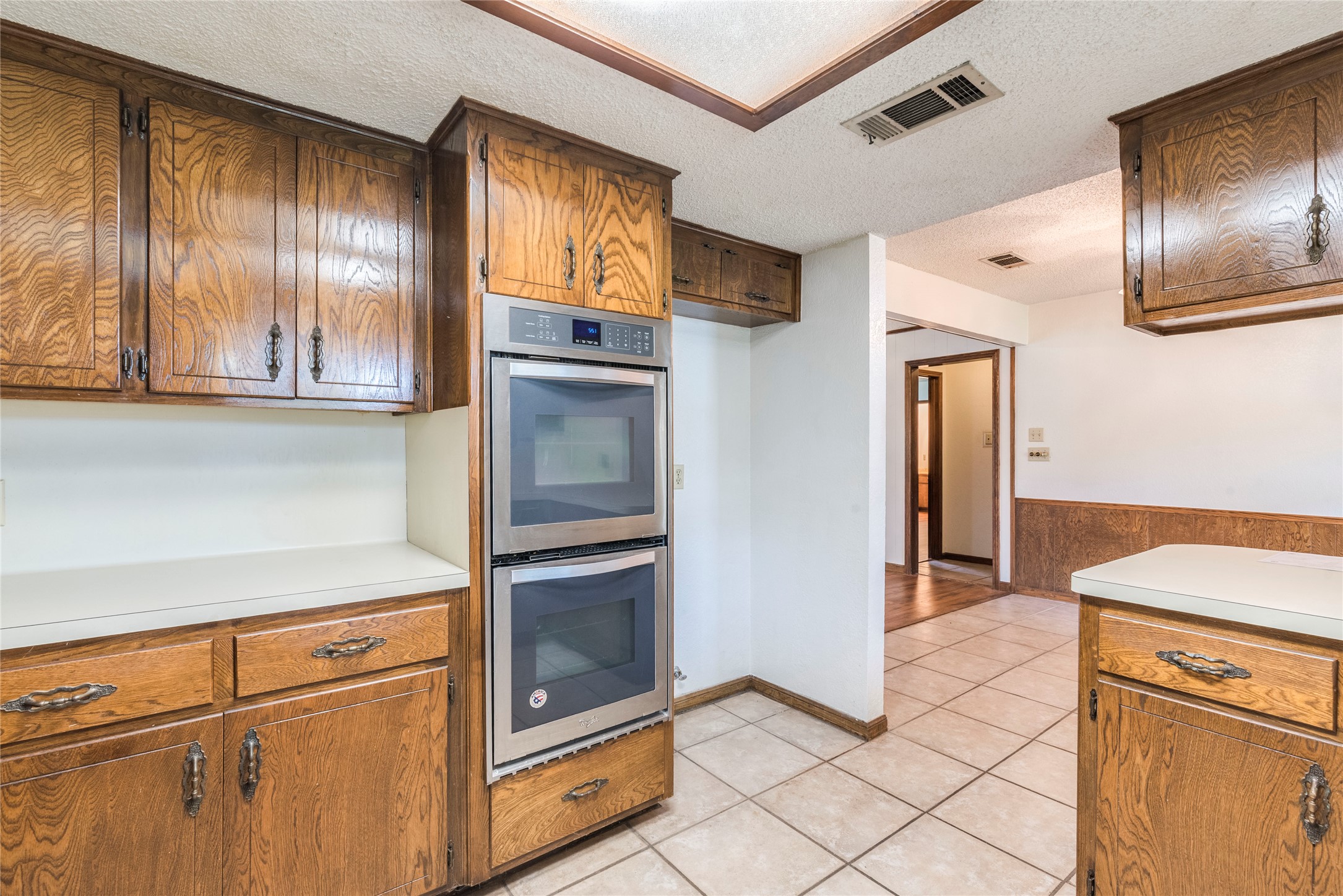 13505 Broadmeade Avenue Austin, TX 78729 - Photo 9 of 21 Kitchen featuring a textured ceiling, stainless steel double oven, light countertops, wood finish cabinetry, and a wainscoted wall