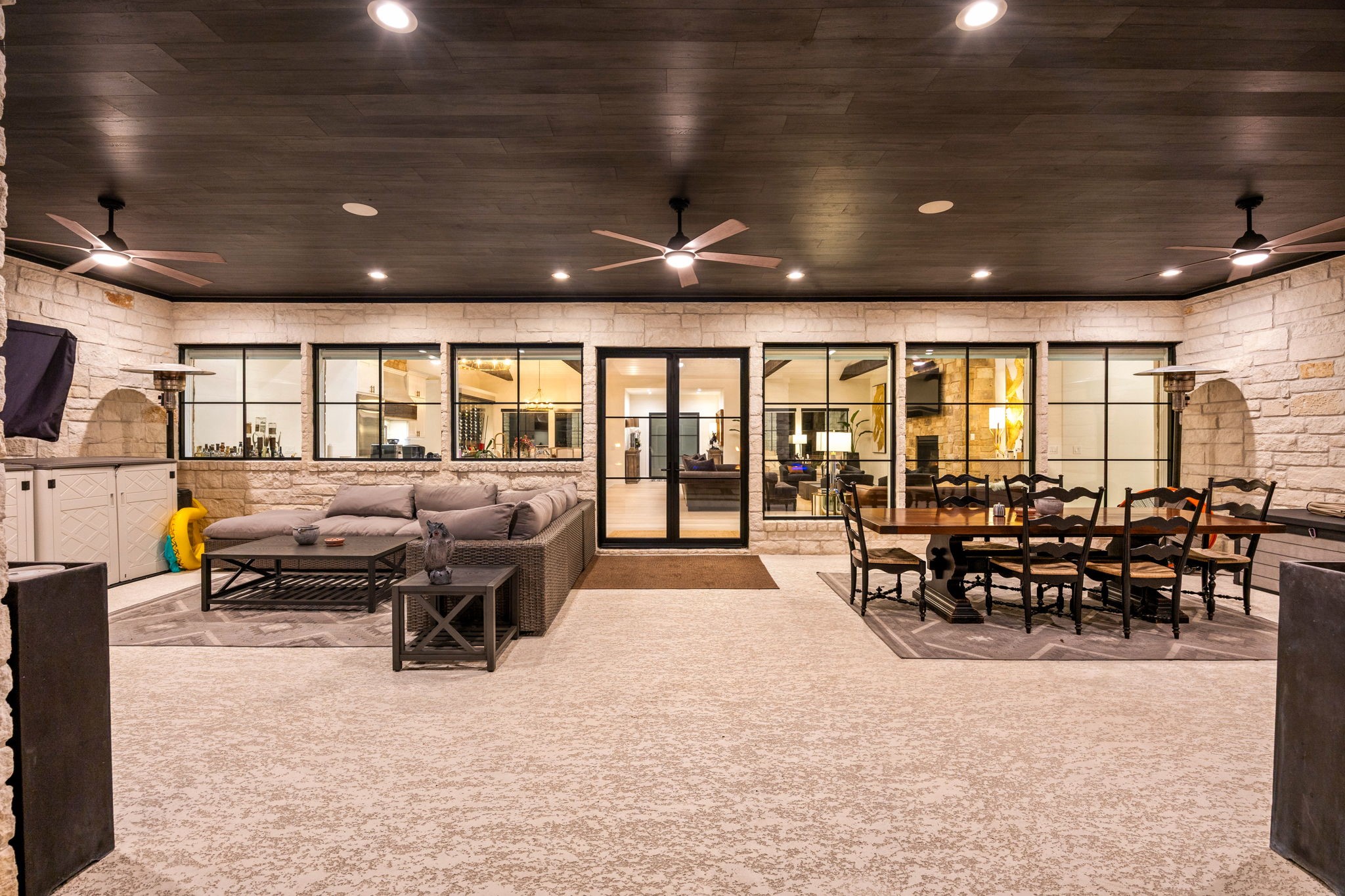 1100 Felder Road Washington, TX 77880 - Photo 41 of 50 The expansive covered patio extends the home's living space outdoors, with multiple ceiling fans, a full outdoor dining area, and a lounge setup — all opening directly to the kitchen and living areas through walls of glass.