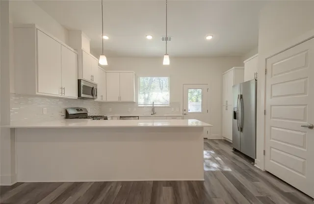 a large kitchen with stainless steel appliances granite countertop a refrigerator a sink dishwasher a stove and white countertops with wooden floor