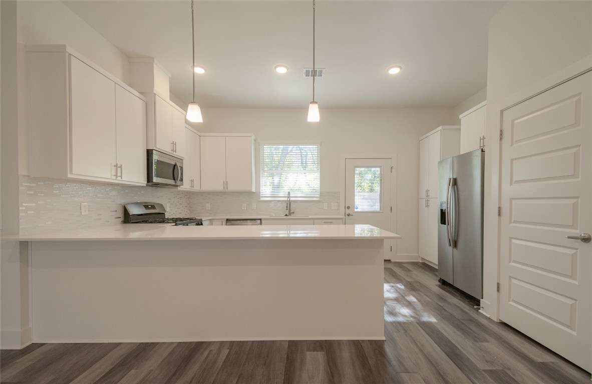 6325 Ponca Street, Unit A Austin, TX 78741 - Photo 7 of 21 a large kitchen with stainless steel appliances granite countertop a refrigerator a sink dishwasher a stove and white countertops with wooden floor