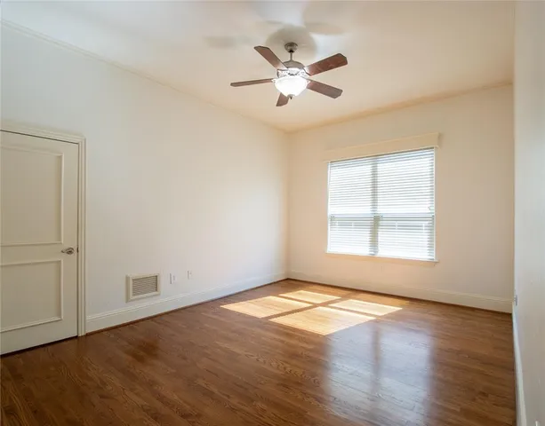 an empty room with wooden floor fan and windows