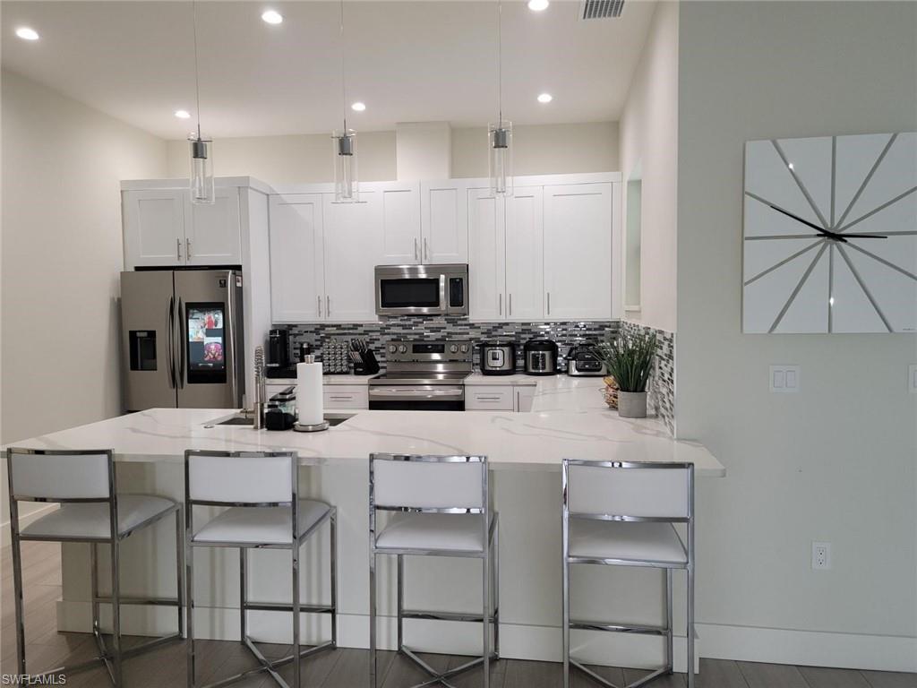 1720 46th Terrace Southwest Naples, FL 34116 - Photo 13 of 24 Kitchen featuring white cabinetry, light stone counters, appliances with stainless steel finishes, a kitchen breakfast bar, and backsplash